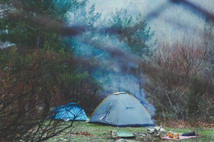 A stunning view of a grey and blue tent amidst a forest with mountains in the background.