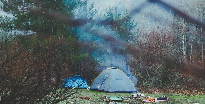 A stunning view of a grey and blue tent amidst a forest with mountains in the background.