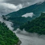 Breathtaking view of a stream of water flowing through lush green mountains under clouds.