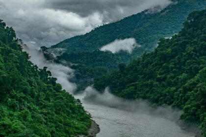 Breathtaking view of a stream of water flowing through lush green mountains under clouds.