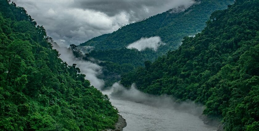 Breathtaking view of a stream of water flowing through lush green mountains under clouds.