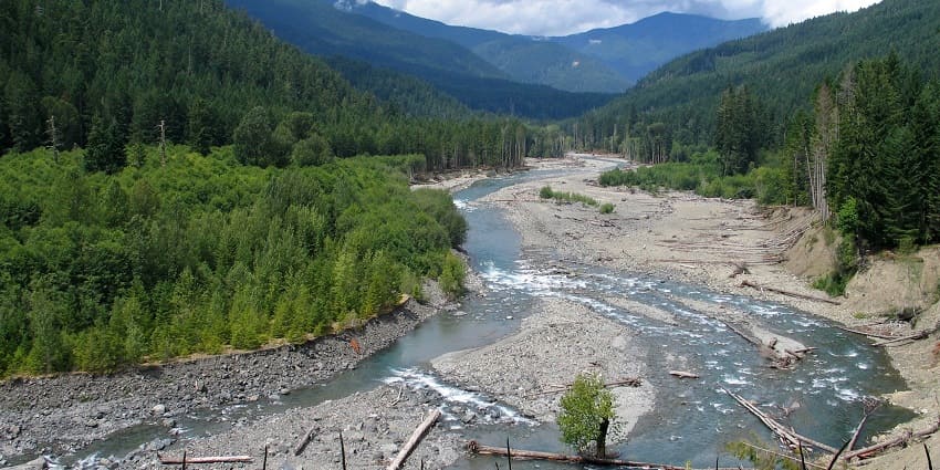 A picture of an almost dried-up river flowing through a valley among tall green mountains
