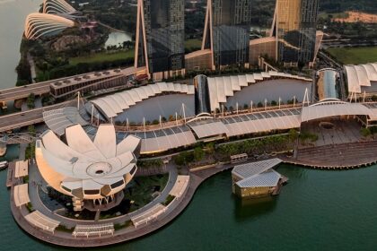 An aerial view of Singapore with tall skyscrapers and lush greenery surrounded by water.