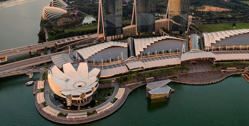 An aerial view of Singapore with tall skyscrapers and lush greenery surrounded by water.