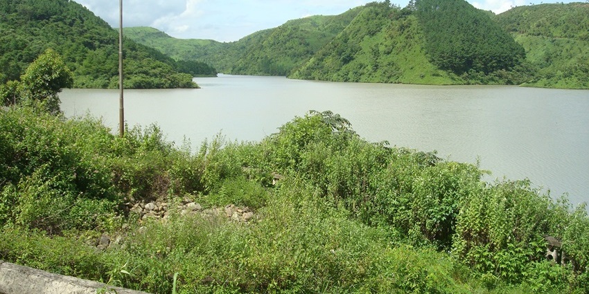 A serene view of the shimmering waters of Singda Dam surrounded by lush greenery.