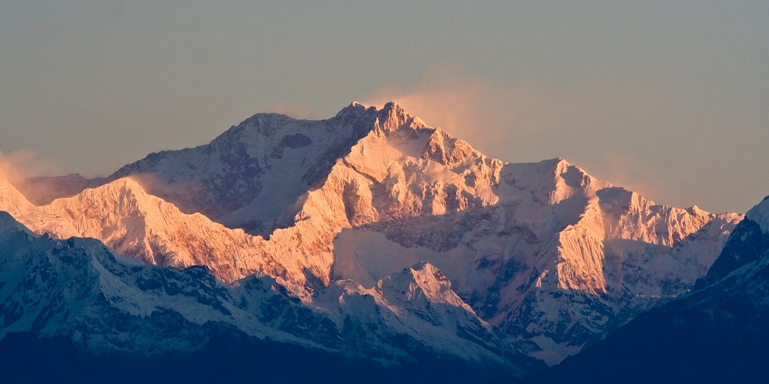 A scenic view of snow-clad mountains with misty air casting an enchanting sunset.