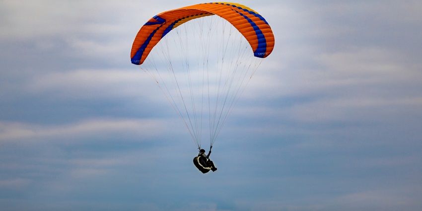 Individual gliding through the air on a parasail under overcast skies.