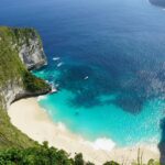 An aerial view of a beach in Bali showing a cliff and the green island