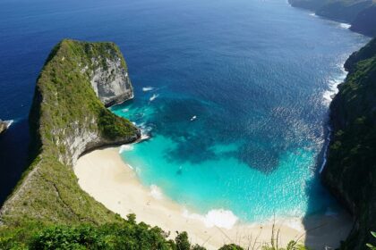 An aerial view of a beach in Bali showing a cliff and the green island