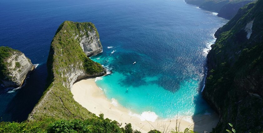 An aerial view of a beach in Bali showing a cliff and the green island