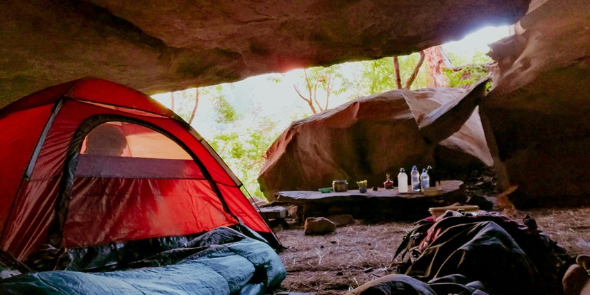 A splendid view of a person sitting in an orange camping tent under a cave during the day.