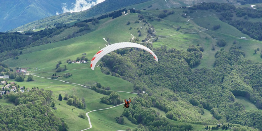 Paraglider soaring over a green valley, with stunning views of rolling hills and skies.