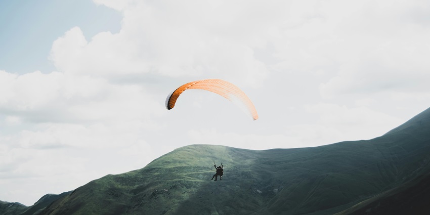 Person on a parachute, gliding through the sky with expansive landscapes and a clear horizon below.