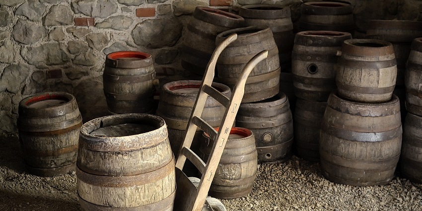 A picture of multiple wooden drums kept on the floor made of rocks in an old brewery.