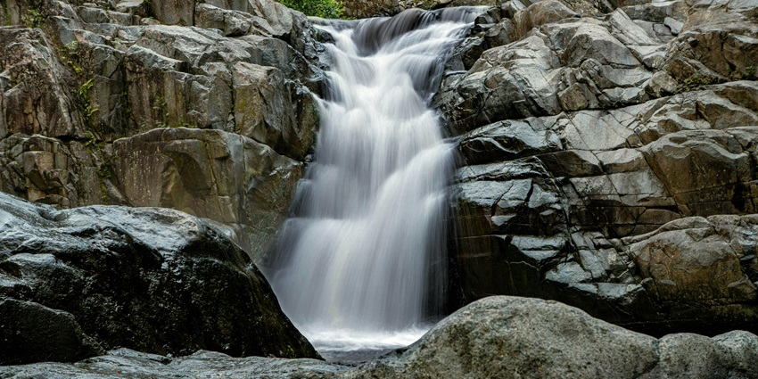 Serene waterfall cascading down rocky cliffs surrounded by lush green forest foliage.