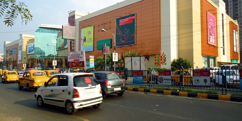 A view of a busy road with different cars in front of South City Mall during the daytime.