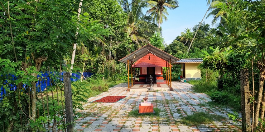Image of a small temple surrounded by lush greenery under clear blue sky during day time view