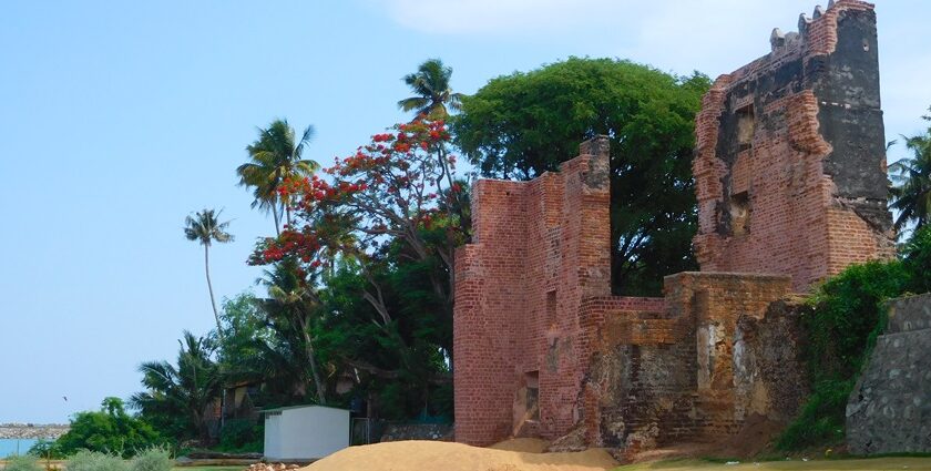 An image of a red wall of a fort surrounded by trees, with a sea nearby