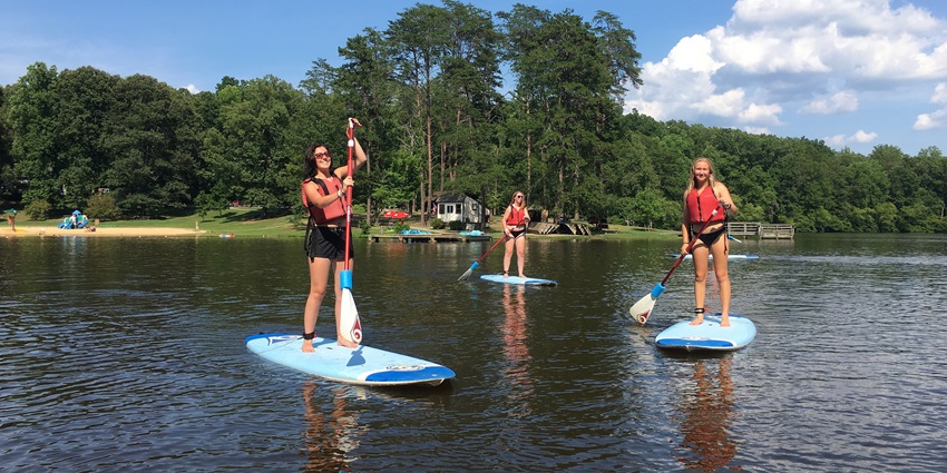 Women enjoying stand-up paddleboarding in a pond surrounded by trees and greenery