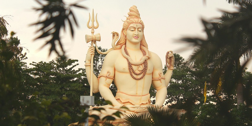 A majestic Lord Shiva statue nestled among lush green trees, radiating tranquility.