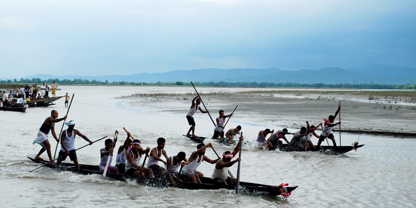 A picture of a boat race ritual happening at a river in Goalpara, with multiple boats participating
