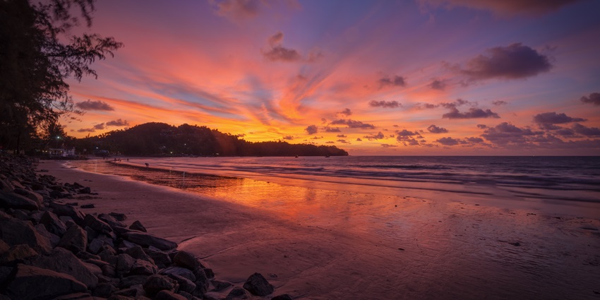 Stunning sunset at Bang Tao Beach with golden skies reflecting on calm ocean waters.