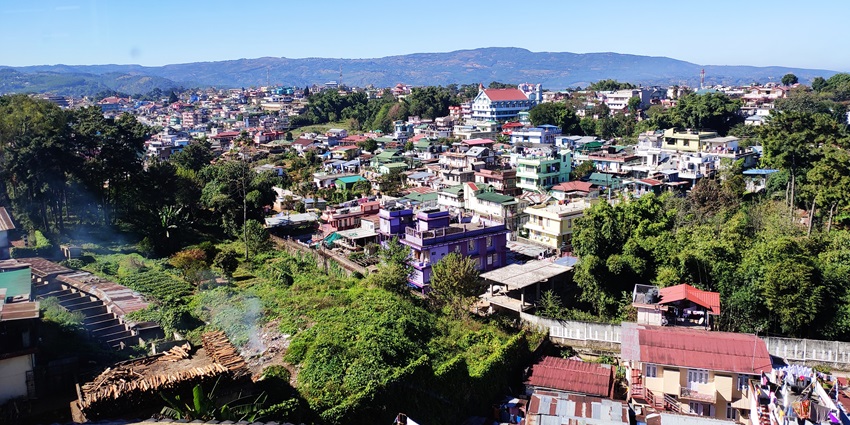 Shillong city view with clustered houses, greenery, and rolling hills under cloudy sky
