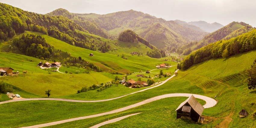 A breathtaking view of a lush green meadow with some houses in the middle during the day.