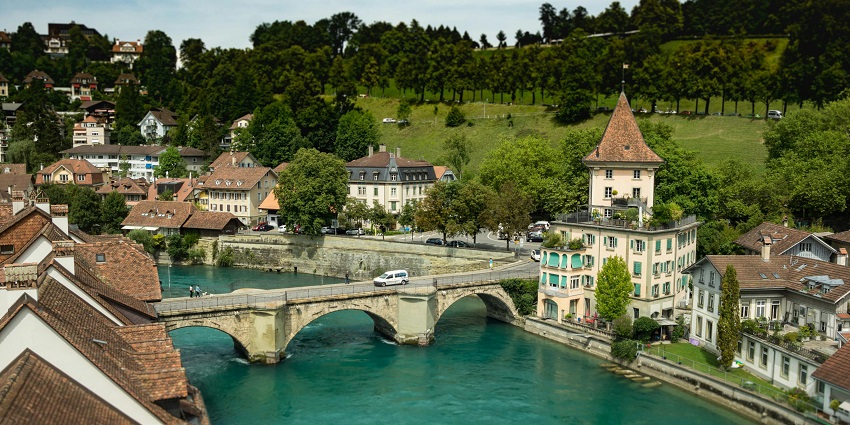 A view of a car on a concrete bridge handing over a water body with houses on each side.