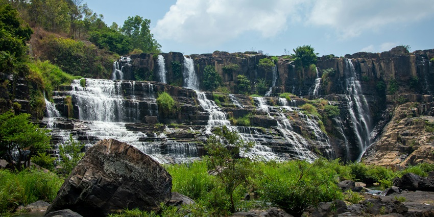 Water gently cascading down a rocky cliffside into a forested ravine