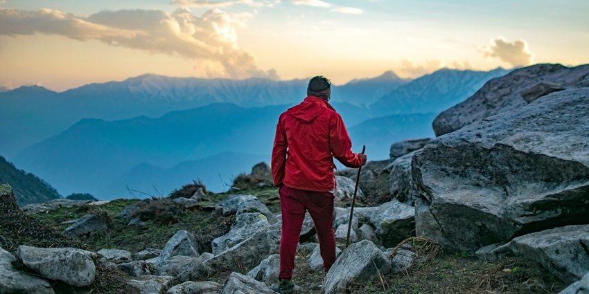 Man in a red hooded jacket and pants holding a black stick, preparing for a hiking adventure.