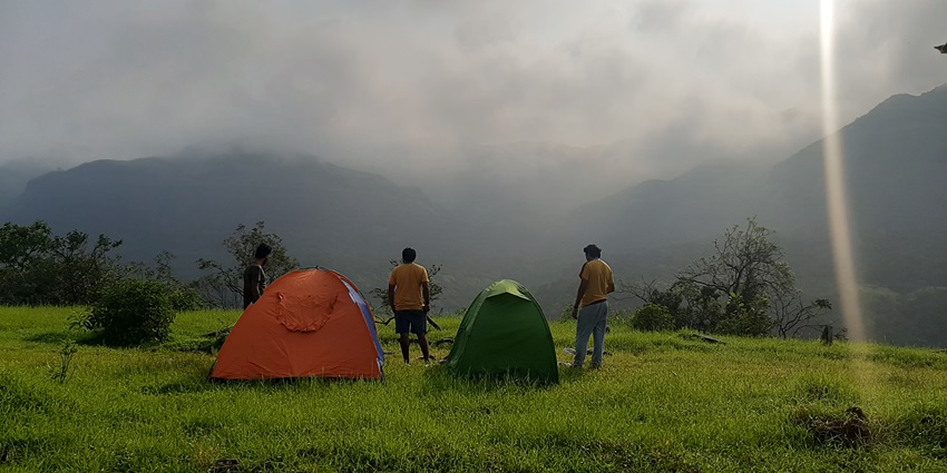 A picture of tourists enjoying a camp on top of a lush hill, surrounded by greenery