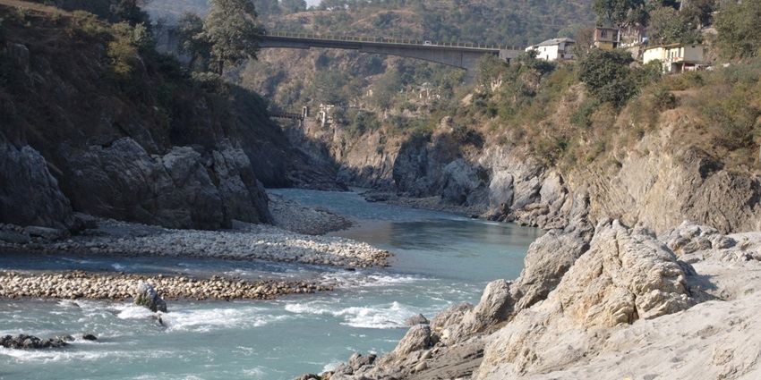 A picture of a river flowing through the rolling meadows with a river crossing bridge in the background