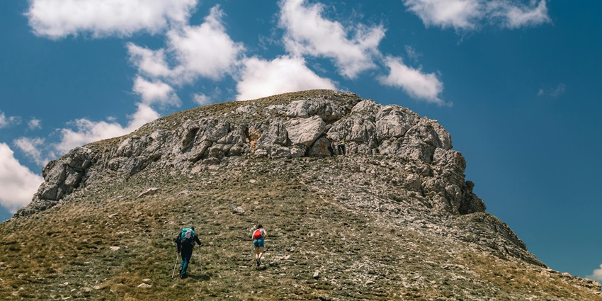 A quaint view of two people hiking their way up to the majestic peaks surrounded by mist.