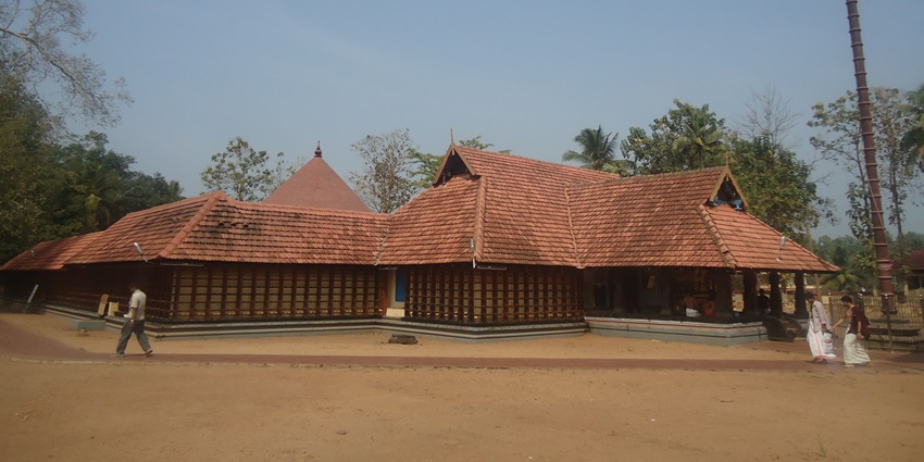 A picture of a temple in Kerala with a red coloured hut-like roof and trees nearby