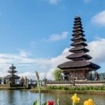 A breathtaking view of two temples on a body of water surrounded by plants and flowers.