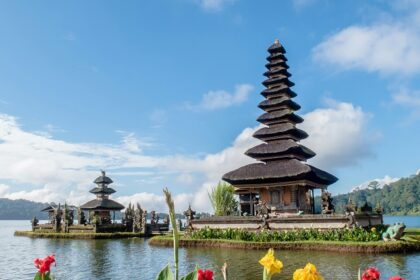 A breathtaking view of two temples on a body of water surrounded by plants and flowers.