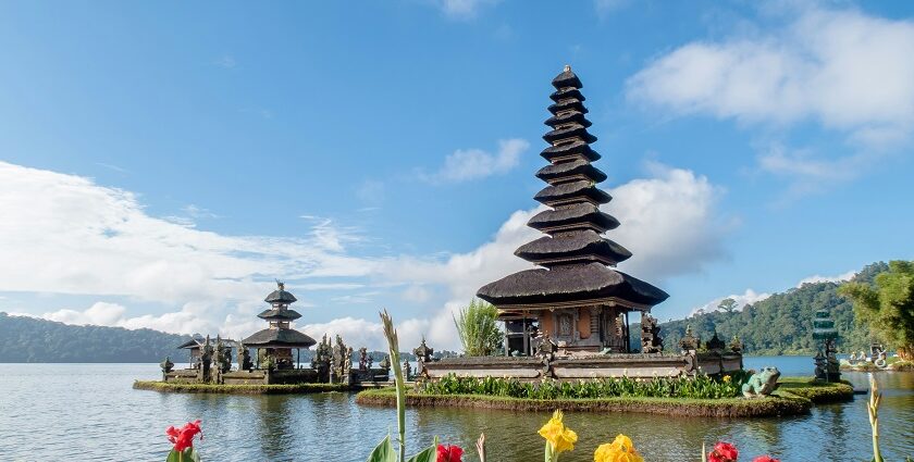 A breathtaking view of two temples on a body of water surrounded by plants and flowers.