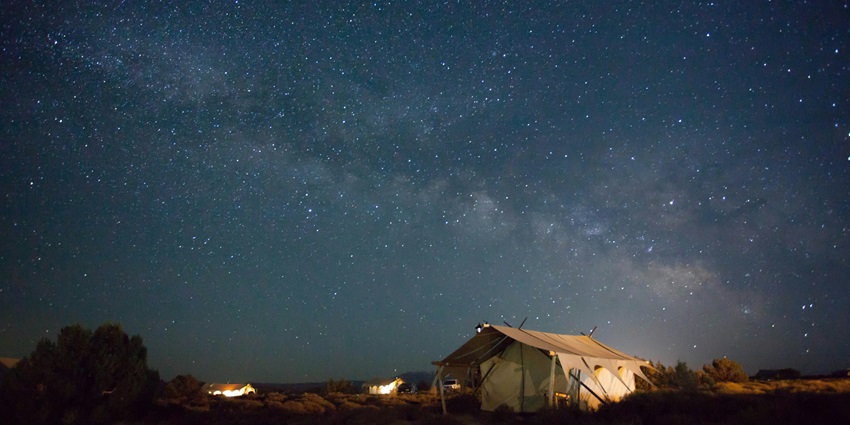 Tent under a starry night sky, surrounded by nature, with soft ambient light illuminating it.