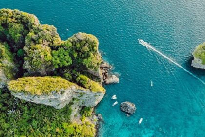 Miltiadis Fragkidis / Unsplash Alt Text: A view of turquoise-blue waters of Phi Phi Islands meeting the lush green surroundings.