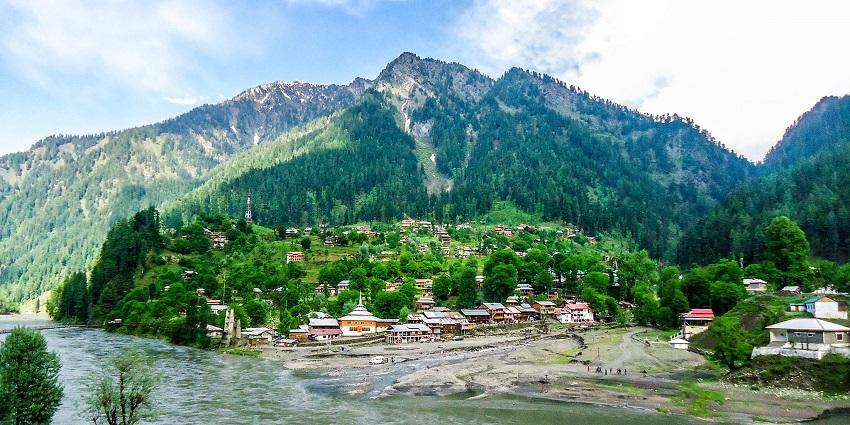A scenic view of a town in Kashmir with lush greenery, located by the side of a river.