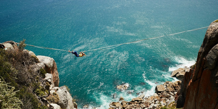 Panoramic image of a man crossing the gorge through azip line amdist the ciffs