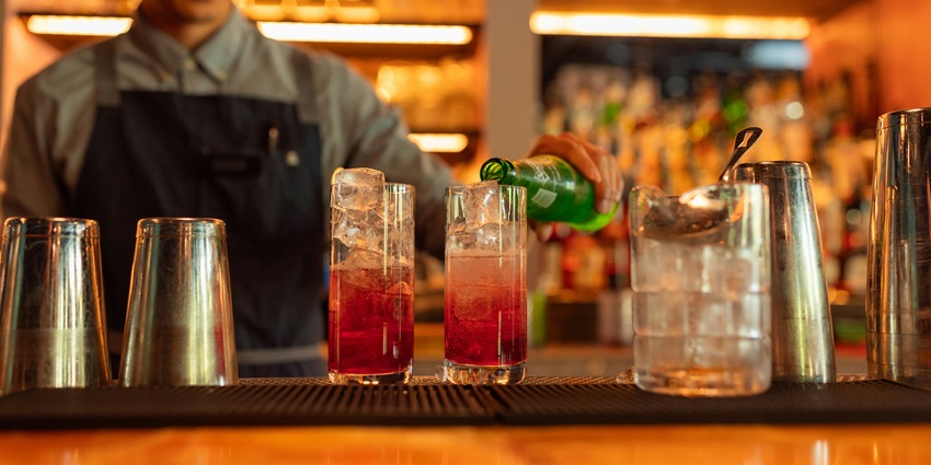 Image of a bartender making two strawberry drinks with ice and mixing soft drink in the glass