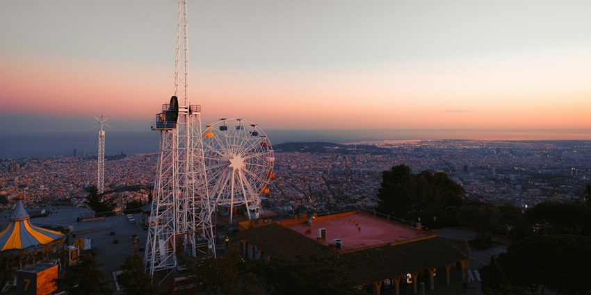 Amusement park rides silhouetted against a vibrant sunset over a coastal city.