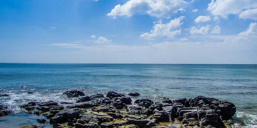 A rocky beach with the sea in front of it, water shining on a sunny day