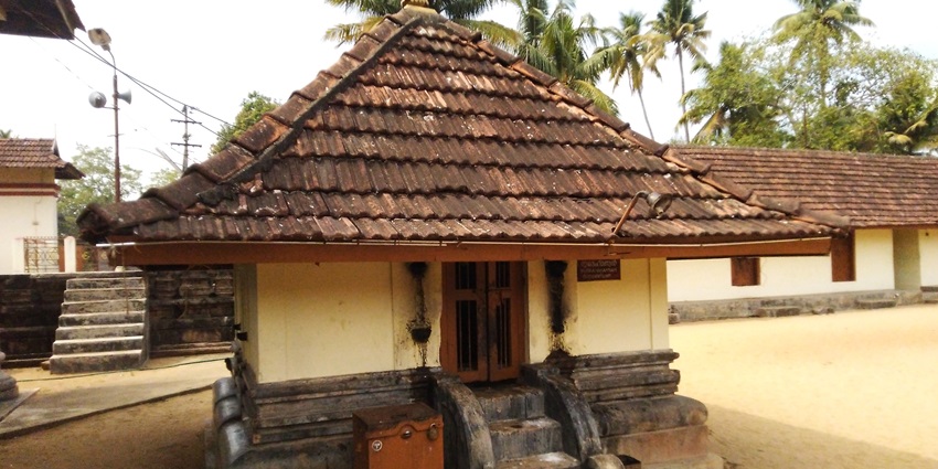 A frontal view of a temple in Kodungallur with tall pine trees in the background
