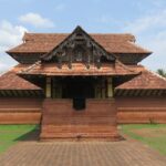 A frontal view of a temple with a hut-like roof with trees and greenery in nearby places