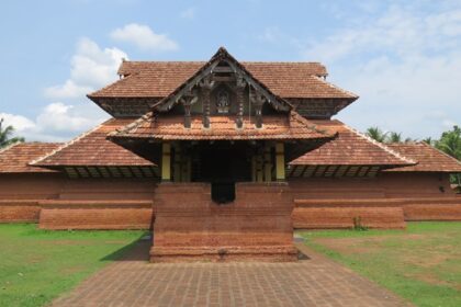 A frontal view of a temple with a hut-like roof with trees and greenery in nearby places