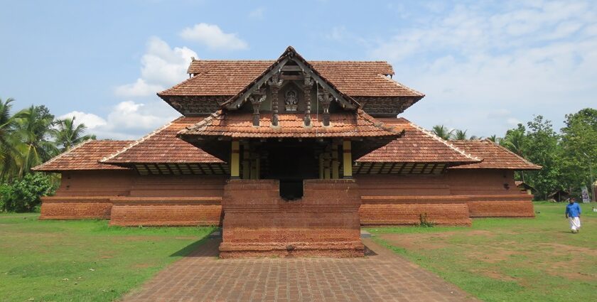 A frontal view of a temple with a hut-like roof with trees and greenery in nearby places