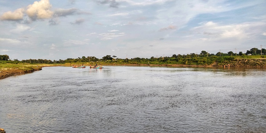 Wide River flows beneath a bright blue sky, flanked by lush green riverbanks.
